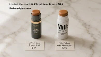 L'Oreal Lumi Bronze Stick in shade Medium next to a Milk Makeup Matte Bronzer Stick in shade Baked. Both are twisted up to show the product. A small handwritten sign says "L'Oreal $14" next to one and "Milk $45" next to the other. Soft natural lighting.