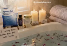 A beautiful bathroom with a bathtub filled with water. Next to the tub are a bag of Epsom salt, a small bottle of lavender essential oil, a jar of coconut oil, a candle, and a folded towel. Steam rises from the water.