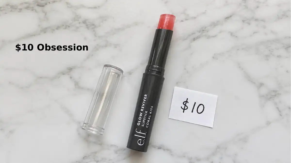 e.l.f. Glow Reviver Slipstick in shade Coral Kiss. The slim twist-up tube with clear cap is shown on a clean white surface. The product is partially twisted up to show the squishy gel texture. A small handwritten tag says "$10". Soft natural lighting.