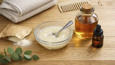 DIY hair gloss treatment in a small glass bowl with a spoon, next to a bottle of clear apple cider vinegar and a sachet of unflavored gelatin, on a wooden bathroom counter – affordable at-home shine recipe for glossy hair.