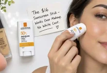 The La Roche-Posay Anthelios UVAir Vitamin Sun Stick SPF50+ in its compact 10ml tube. Next to it, a hand applying the stick over a full face of makeup. A sign says "$16 – Works Over Makeup, No White Cast."