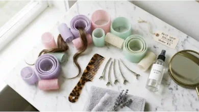 Set of self-grip velcro hair rollers in various sizes arranged on a white marble vanity next to a comb, sectioning clips, and a hairspray bottle – affordable DIY voluminous blowout technique under $5.