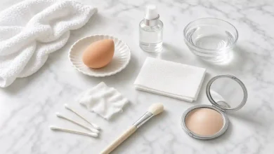 Close-up of a makeup sponge with a spritz of water, a clean tissue, and a damp cotton cloth next to a compact mirror – DIY free household fixes for cakey foundation.