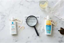 High-end French pharmacy sunscreen next to an affordable drugstore sunscreen on a white marble surface, with UV filter charts and a price tag comparison – budget vs. premium sunscreen effectiveness.